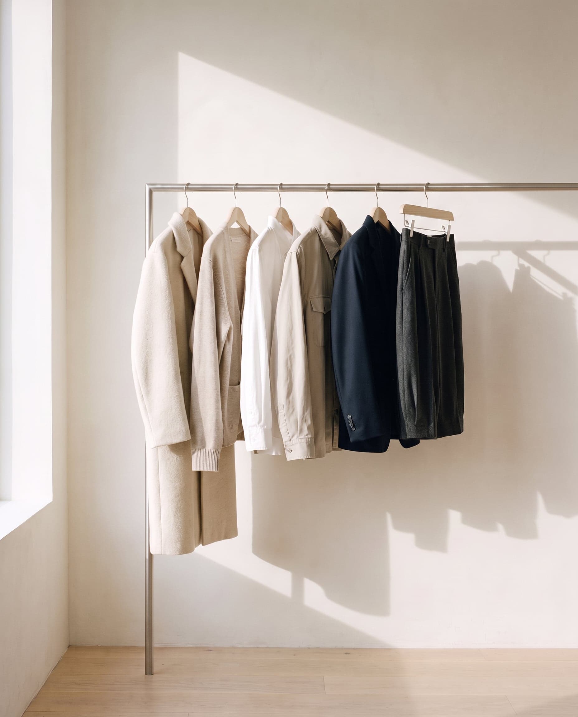 Garments on wooden hangers along a steel rail in a bright studio.