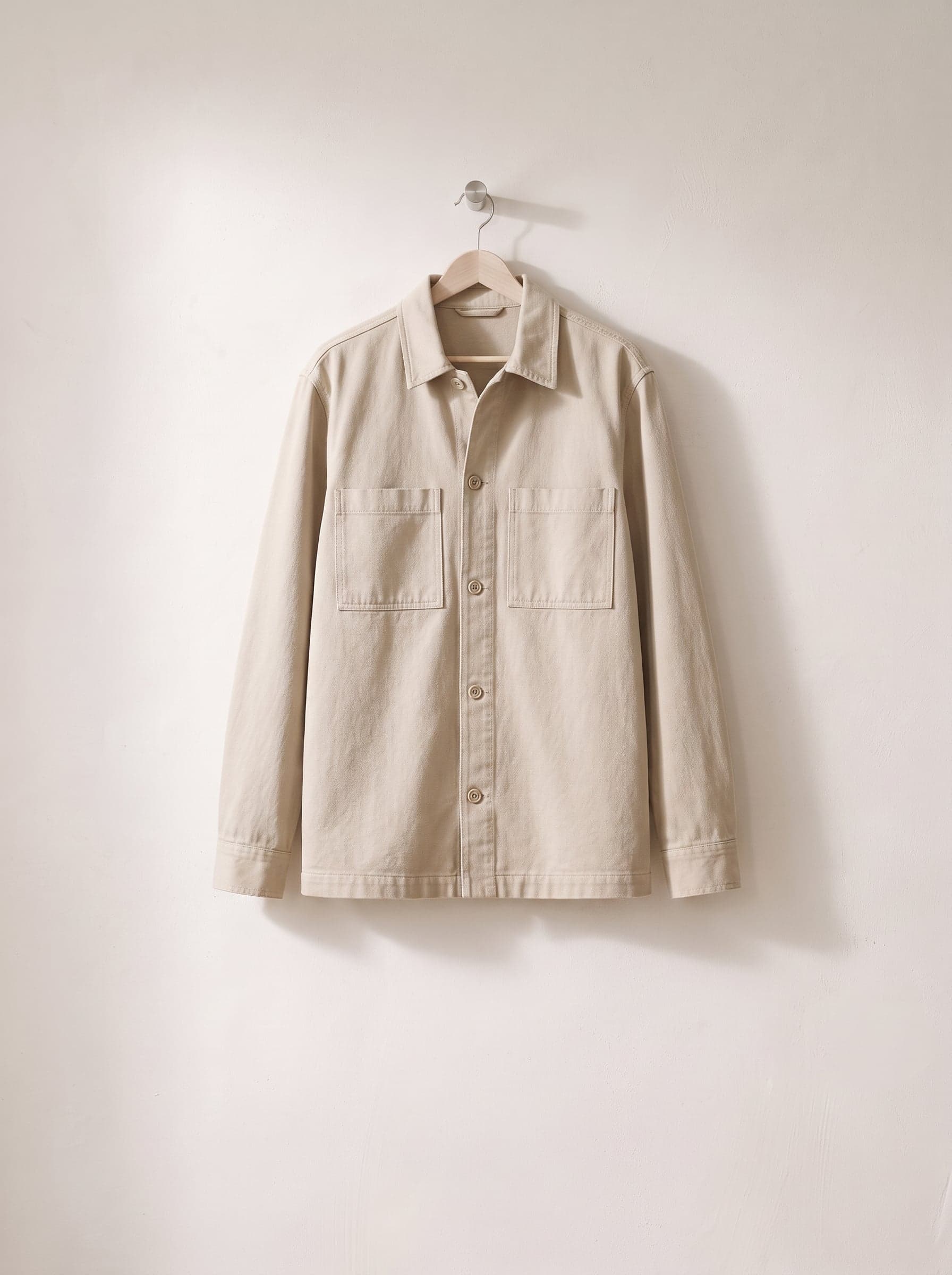Stone-coloured overshirt with two chest pockets on a wooden hanger.