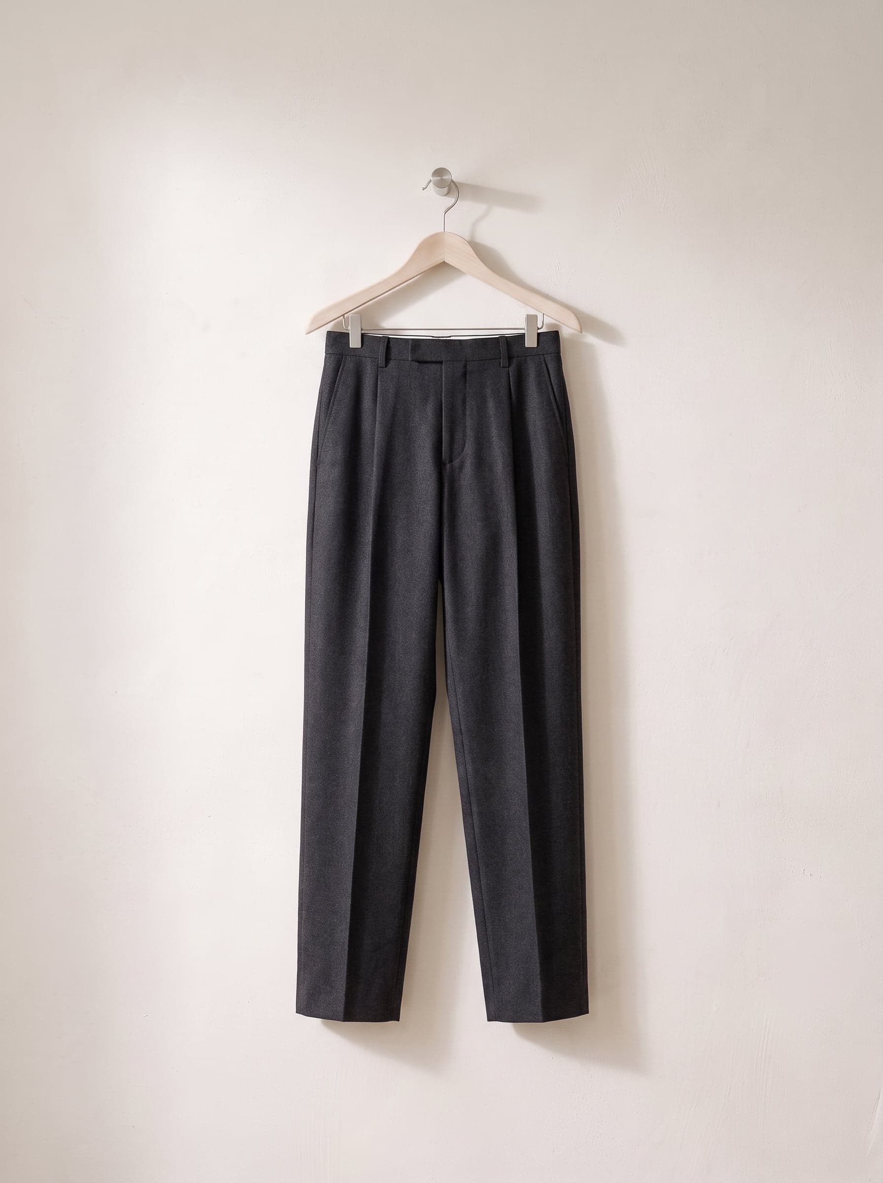 Charcoal pleated trousers on a wooden trouser hanger.