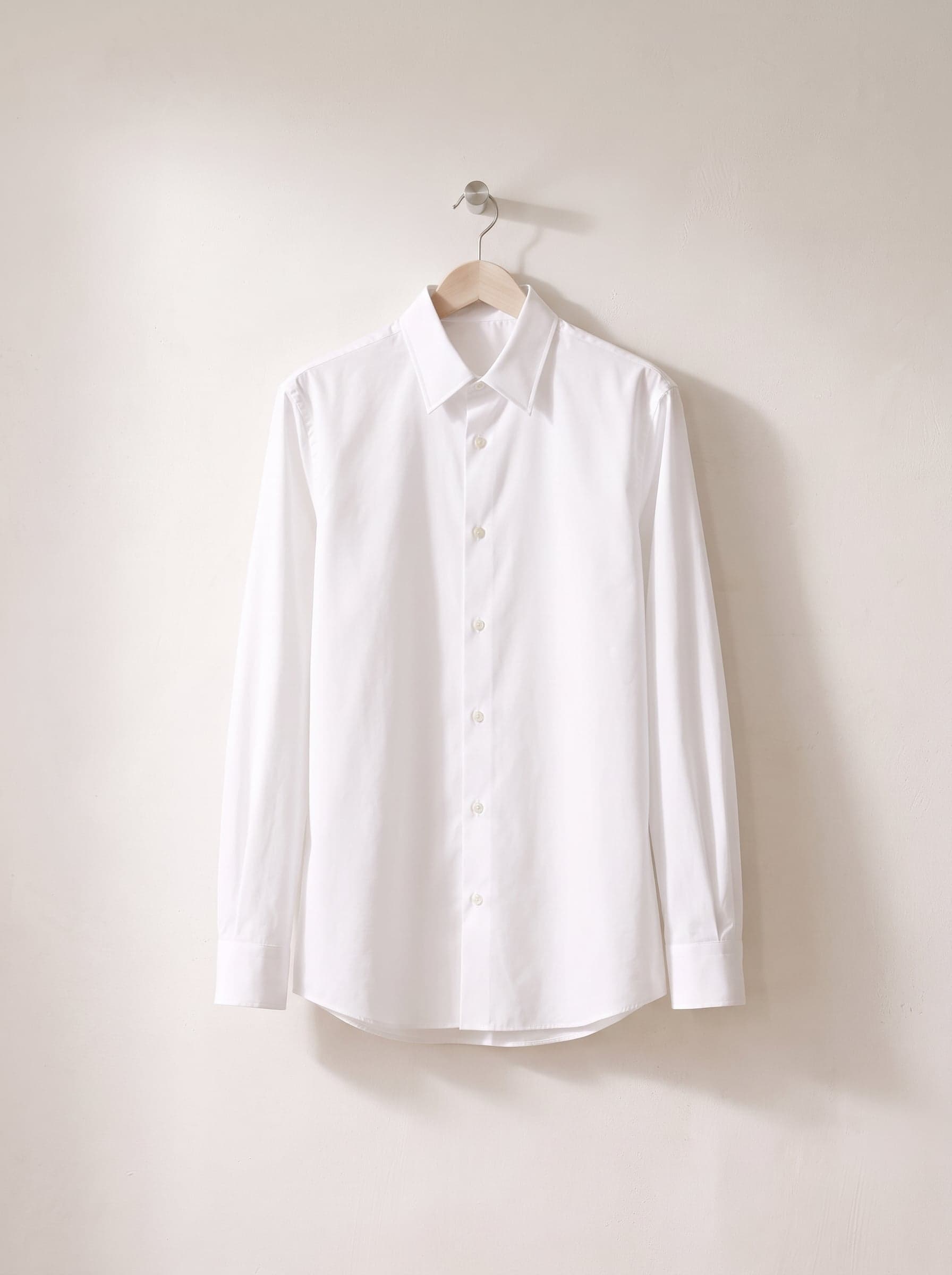 White cotton shirt on a wooden hanger against a white plaster wall.