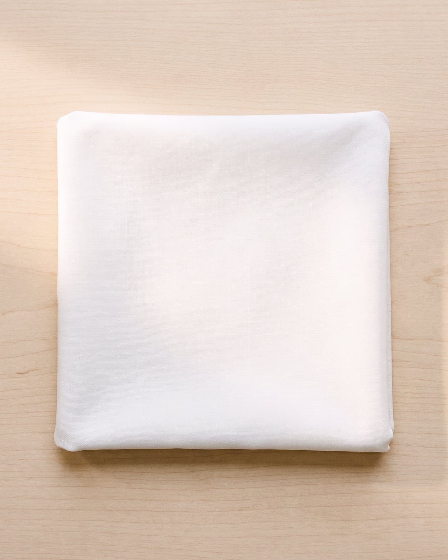 A folded square of white cotton poplin on pale ash wood.