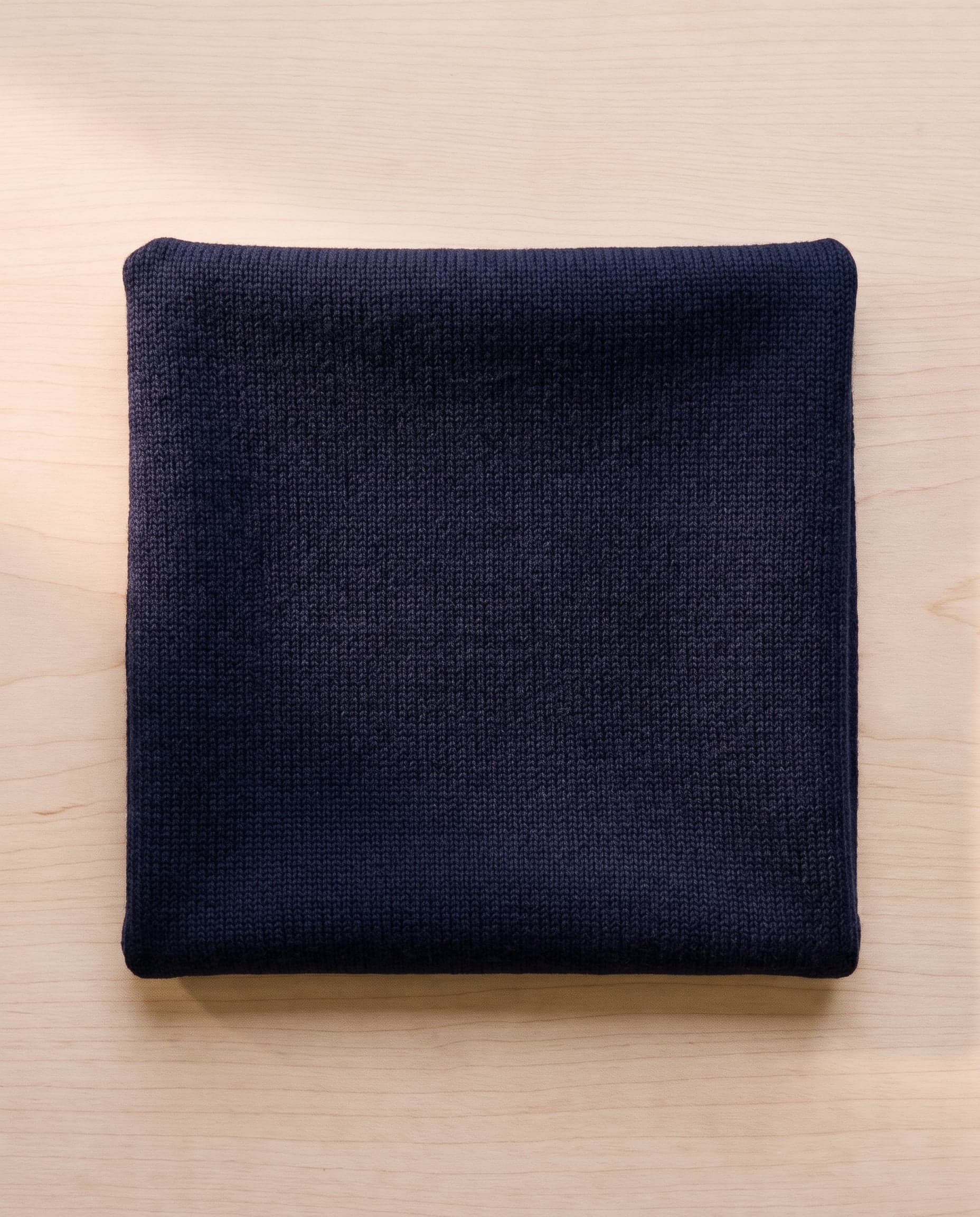 A folded square of navy merino knit on pale ash wood.