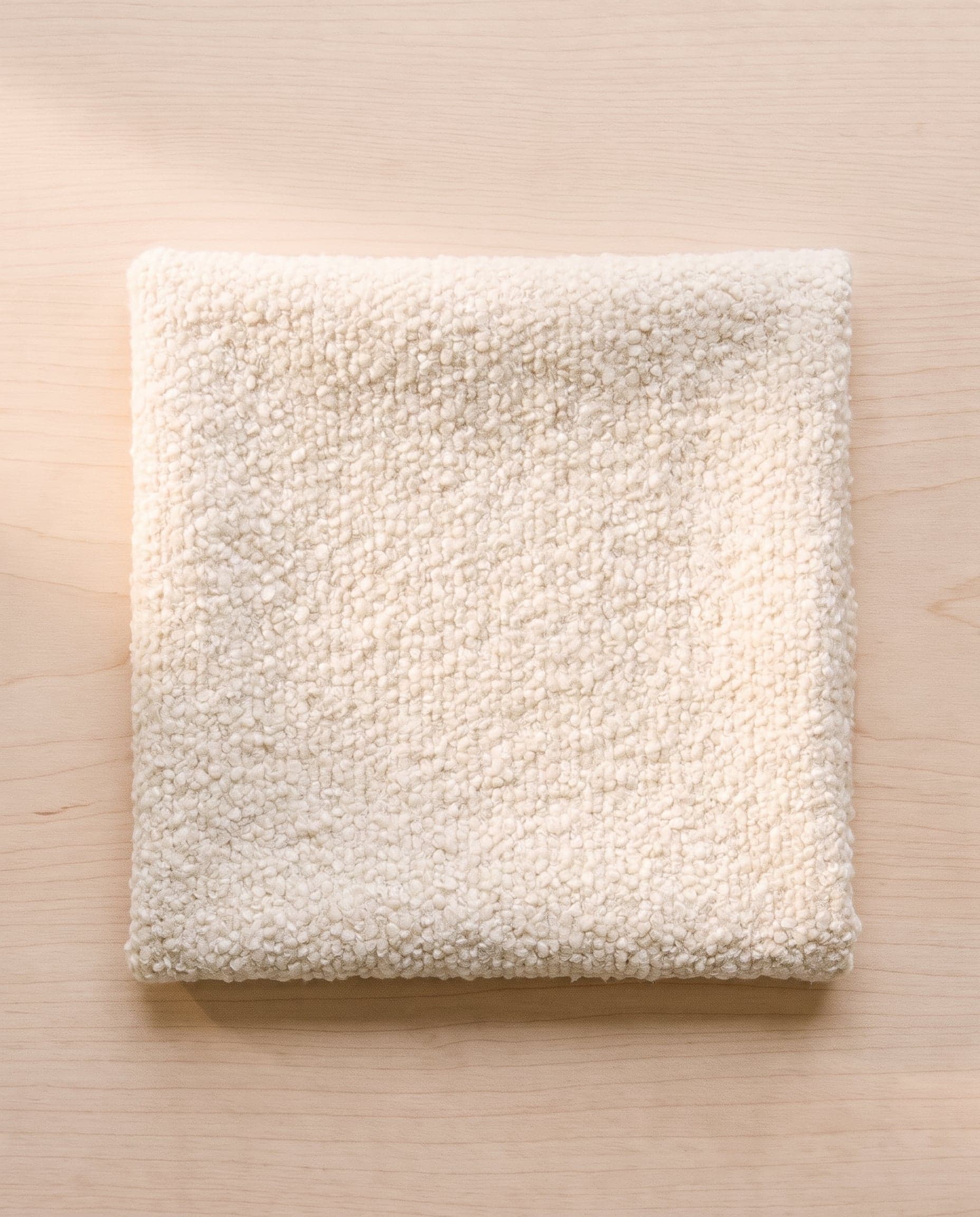 A folded square of ecru wool bouclé on pale ash wood.