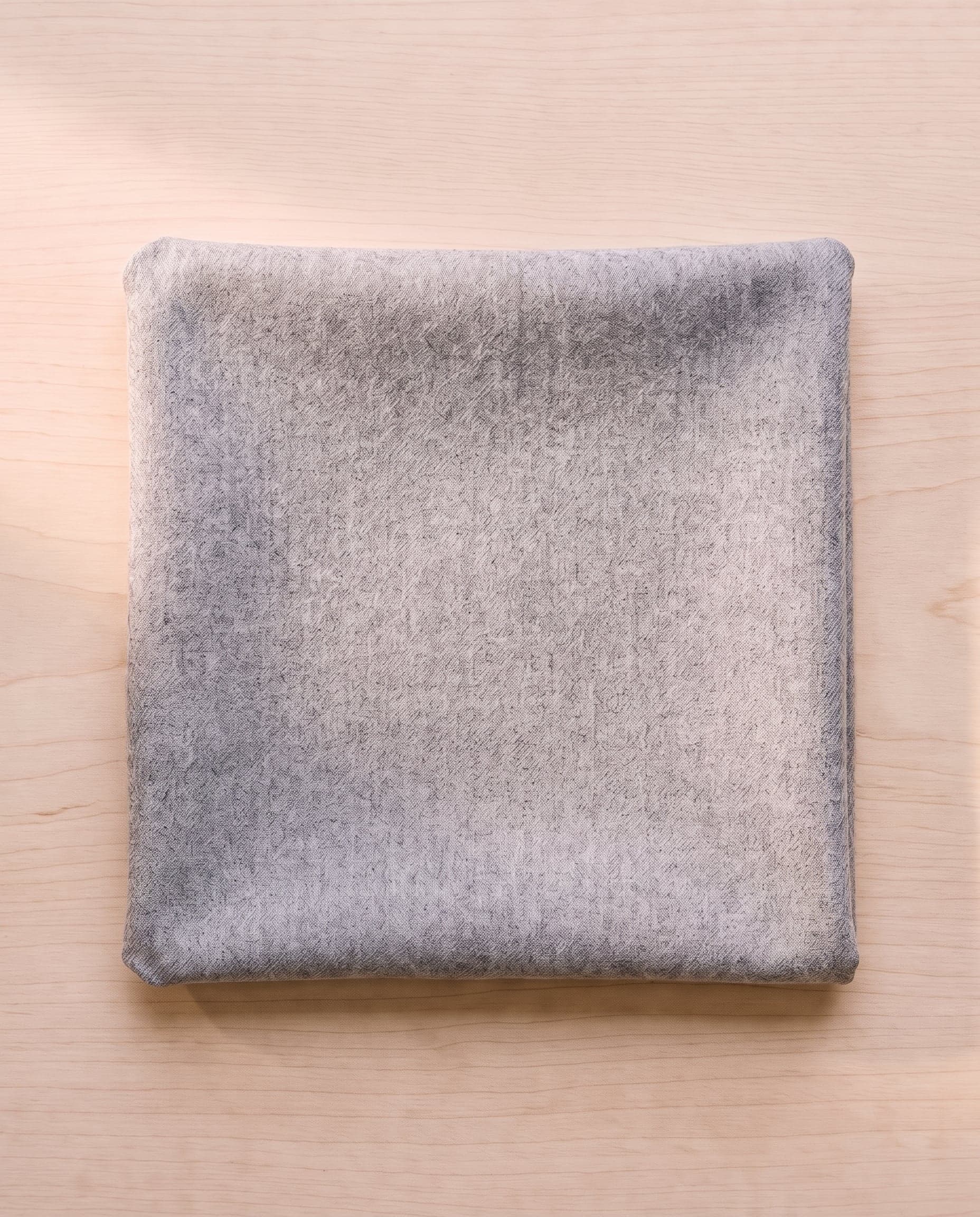 A folded square of grey wool flannel on pale ash wood.